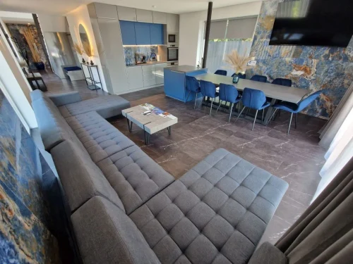 Belső közösségi tér TV-s nappalival, étkezővel és háttérben a konyhával