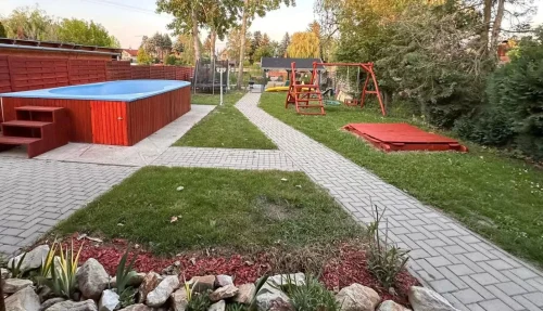 Kilátás a teraszról a vízpartra: 3 x 5 méteres medence, rönkfa játszótér, trambulin