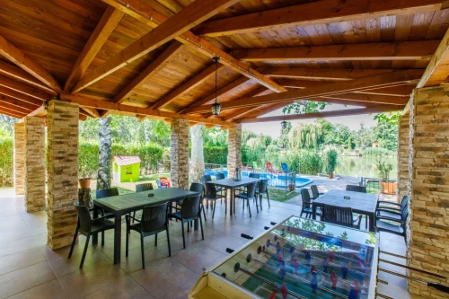 Nagy, fedett terasz kerti bútorokkal, csocsóval, a kertben gyermekjátékokkal